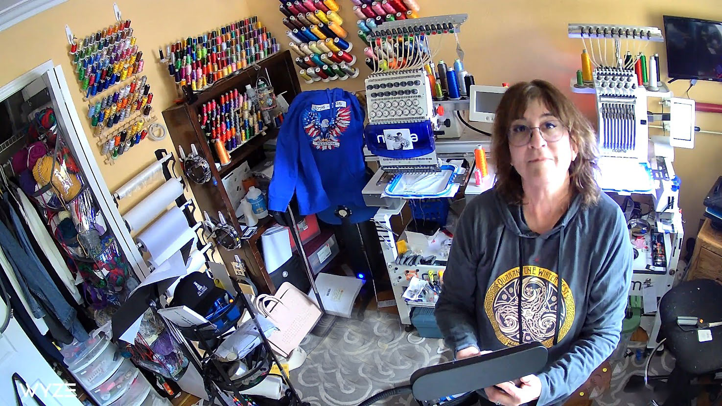 Woman standing in shop with embroidery machines and colorful thread around in the background